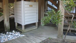 Eine Holzterrasse mit einer weißen Struktur, möglicherweise eine Laube oder ein Abstellraum, und einem kleinen Baum.