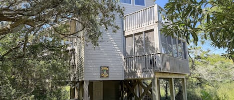 A two-story wooden structure with a balcony, surrounded by dense foliage.