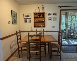 A dining room with a wooden table and chairs, a wall-mounted shelf with decorative items, and framed pictures.