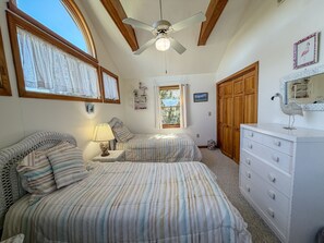 A bedroom with two beds, a ceiling fan, a dresser, and a window with curtains.