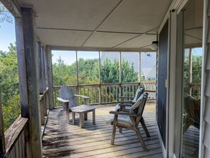 A wooden deck with a table and two chairs, overlooking a forested area.