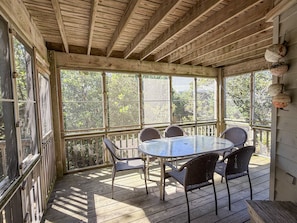 Un espace extérieur abrité, aménagé avec une table ronde et des chaises en osier, de grandes fenêtres et un plafond en bois.