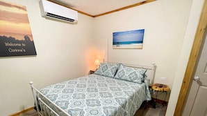 Ein Schlafzimmer mit einem Bett, einem Nachttisch, einer Klimaanlage, einem Wandbild und einer Tür.