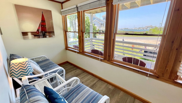 Ein gemütliches Zimmer mit Bett, Stuhl und Fenster mit Blick auf Strand und Segelboot.