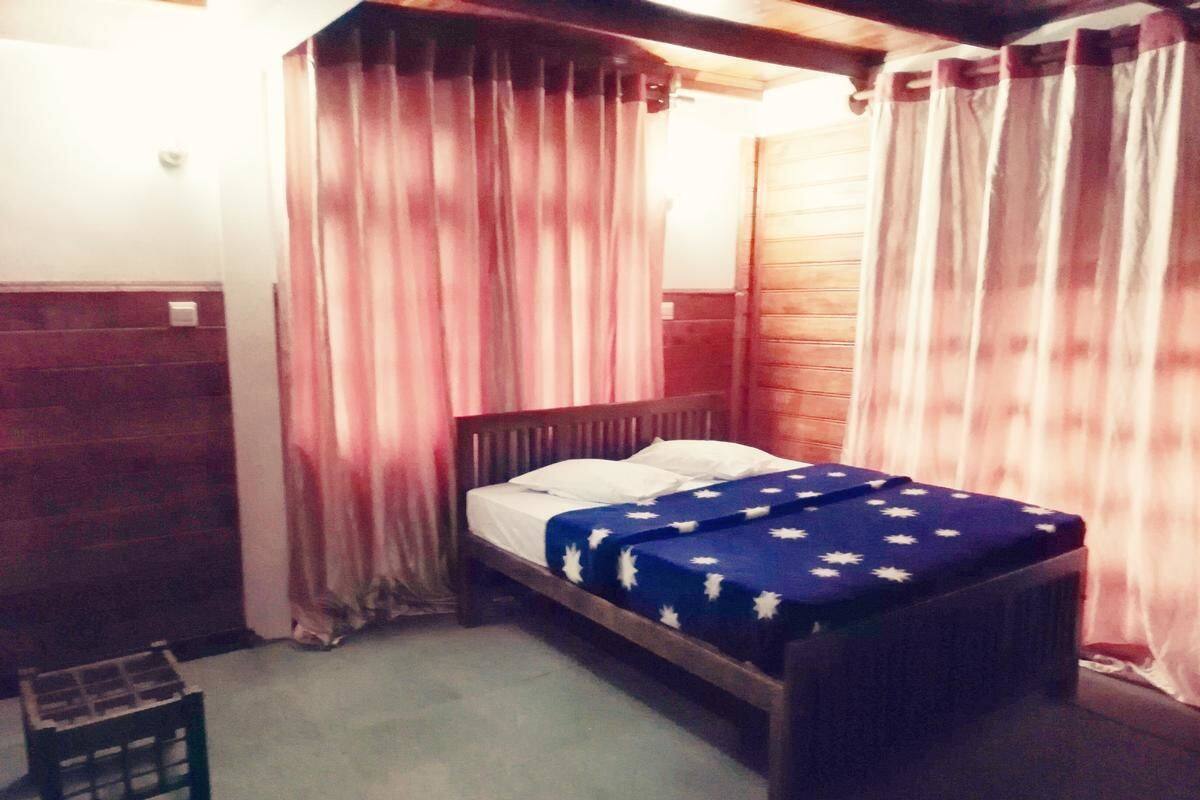 A single bed with a blue bedspread, wooden headboard, and curtains.