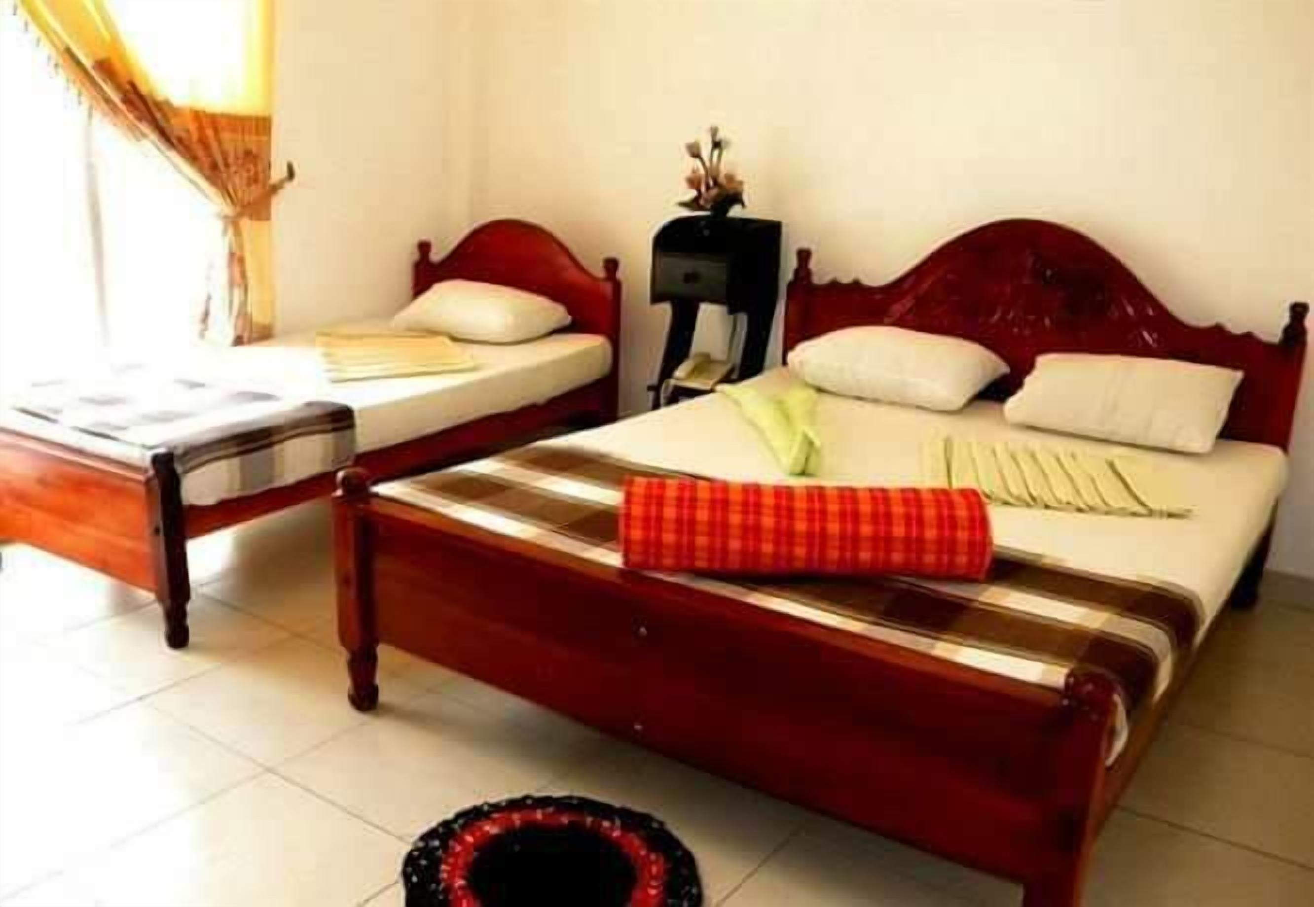A hotel room with two wooden beds, one with a red and white checkered blanket and the other with a green and white blanket.