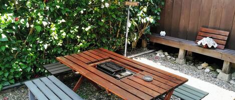 Un'area salotto all'aperto con tavoli e panche in legno, immersa nel verde e delimitata da una recinzione in legno.