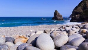 Una playa rocosa con grandes rocas y una formación rocosa destacada al fondo.