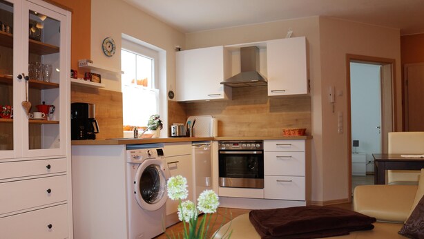 A compact kitchen with a washing machine, oven, and a dining area with a table and chairs. - Cozy apartment near Kronach (Kronach)