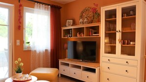 A living room with a TV, a cabinet with glass doors, a sofa, and a small table with a plant. - Cozy apartment near Kronach (Kronach)