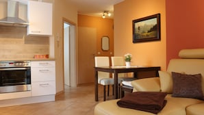 A modern kitchen with a built-in oven and cabinets, a dining area with a table and chairs, and a cozy living space with a sofa and cushions. - Cozy apartment near Kronach (Kronach)