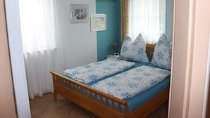 A bedroom with a wooden bed, floral bedding, a nightstand, and a wall-mounted lamp. - Cozy apartment near Kronach (Kronach)