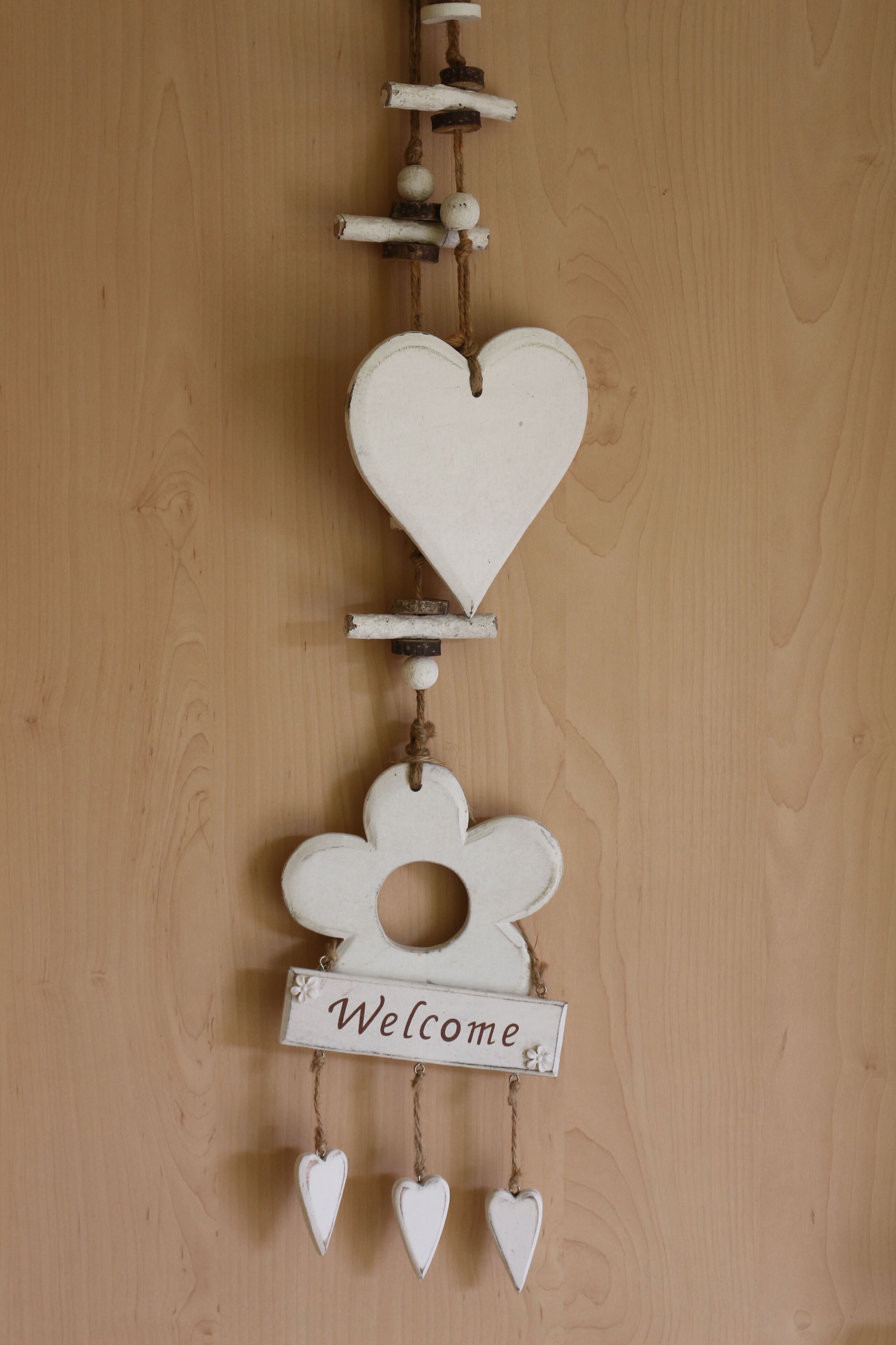 A wooden wall with a decorative hanging featuring a heart, a flower, and a 'Welcome' sign.