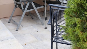 An outdoor patio with a table and two chairs, a small potted plant, and a window with a view of a house. - Cozy apartment near Kronach (Kronach)
