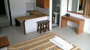 Kompakti hotellihuone, jossa on pieni keittiönurkkaus, pieni kylpyhuone, raidallinen peitto sängyllä ja puinen työpöytä, jossa on peili.