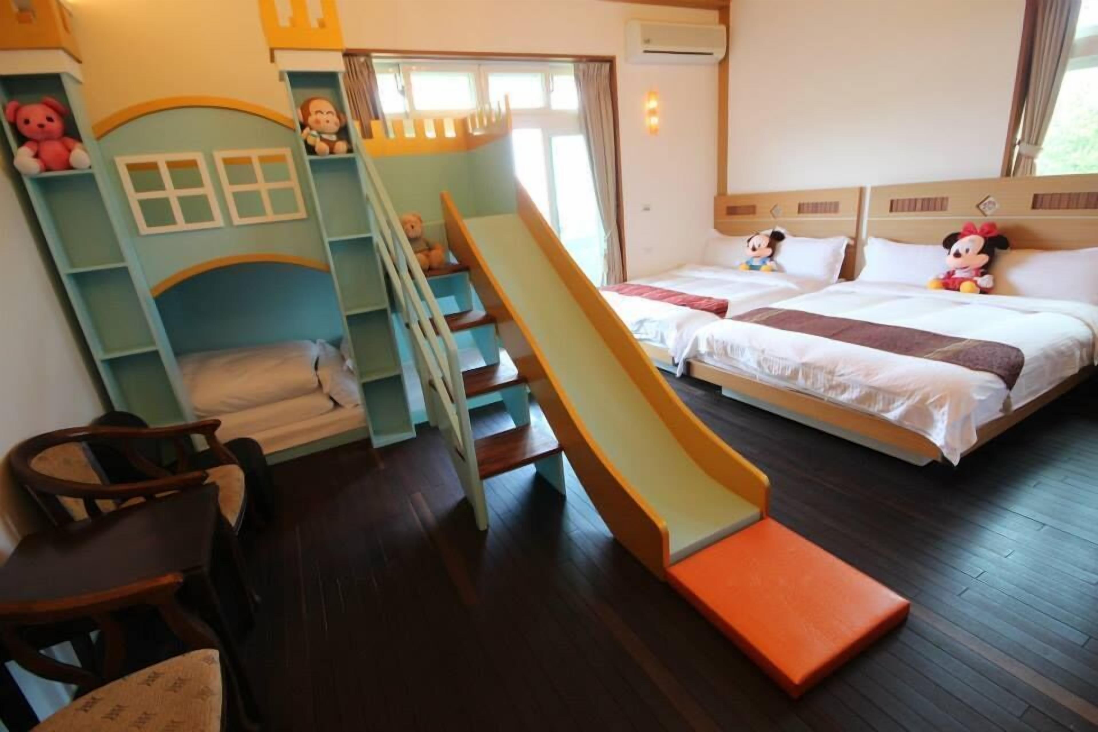 Quarto infantil com escorrega, beliches e brinquedos de pelúcia do Mickey Mouse.