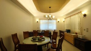 Un comedor con una mesa redonda, sillas, una lámpara de araña y una zona de cocina con refrigerador y microondas.