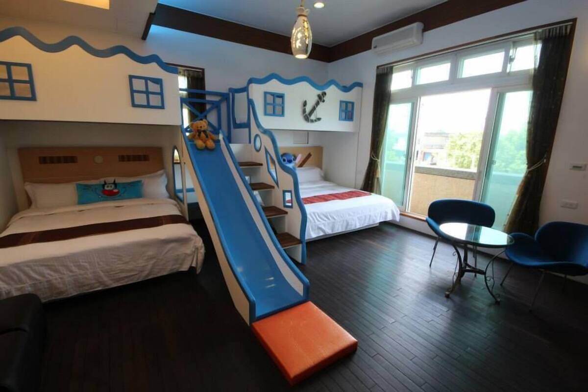 A hotel room with a bunk bed, a slide, a small table, and chairs.