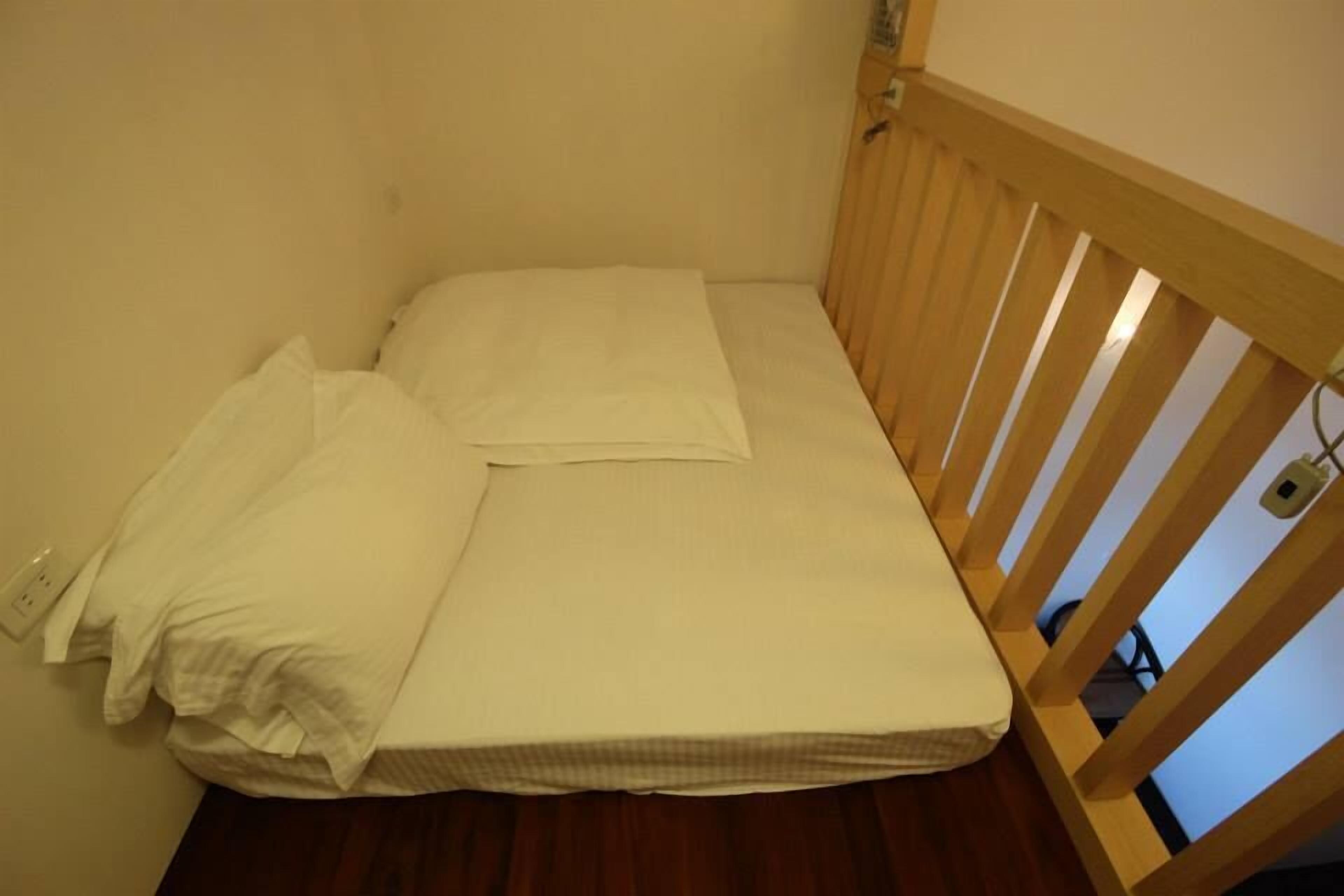 Una habitación pequeña con una cama individual, cabecera de madera y un colchón blanco sencillo.