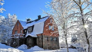 A snow-covered house with a stone foundation and a brick upper section, surrounded by snow-laden trees. - Marston Hill (Mullsjö)