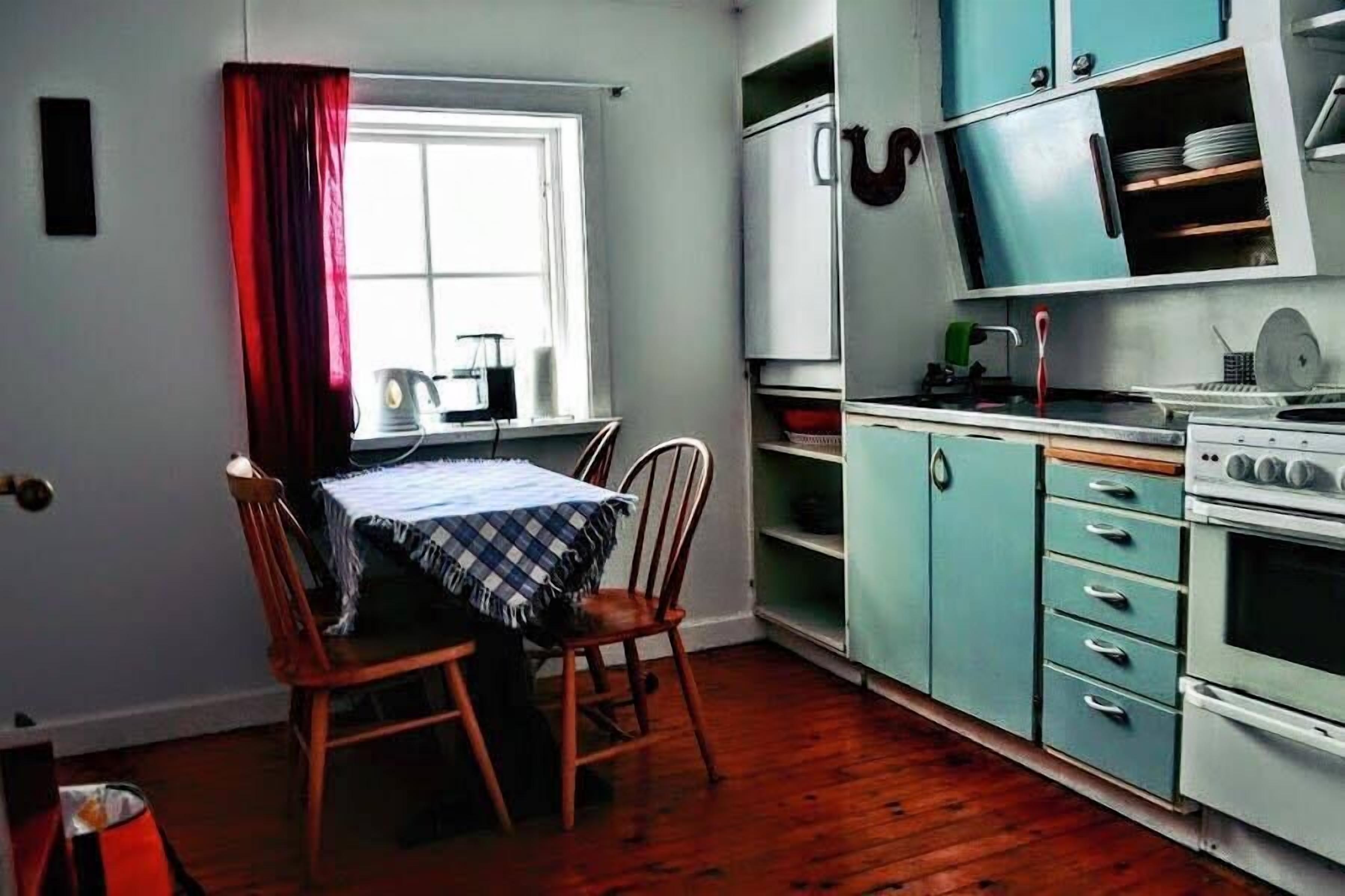 Een kleine keuken met een eettafel en stoelen, een raam met gordijnen, en een fornuis.