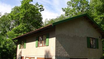 A two-story building with a sloped roof, green shutters, and a dirt ground floor.