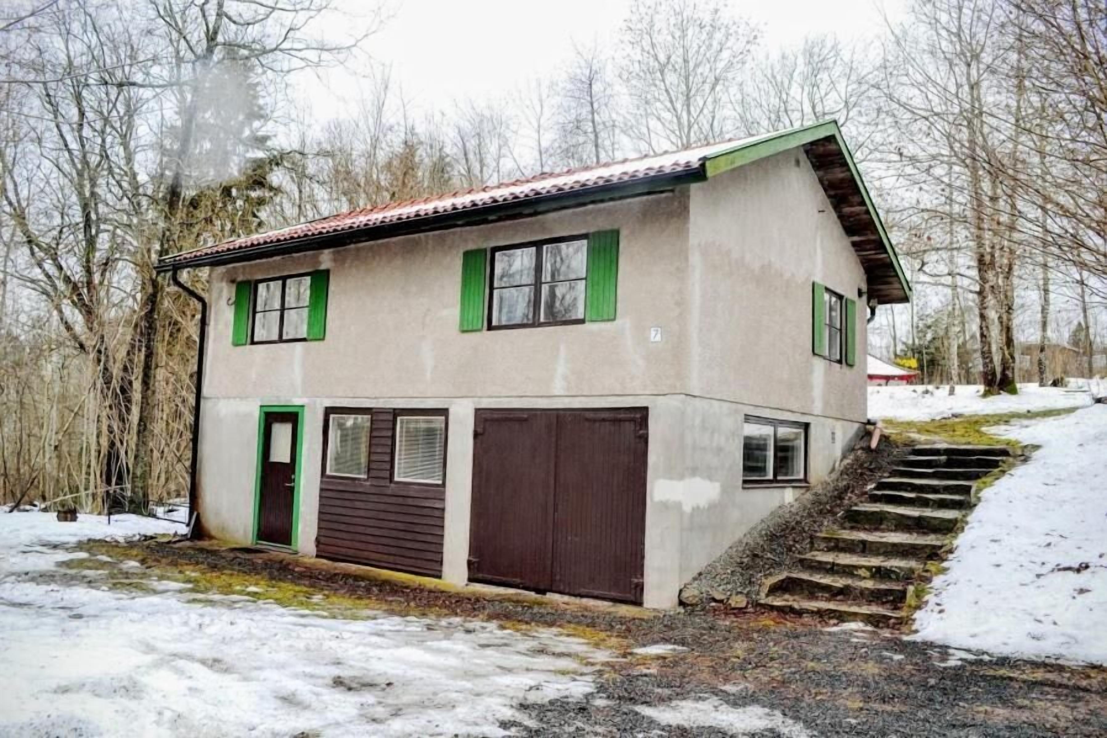 Una casa de dos pisos con techo inclinado, contraventanas verdes y una puerta marrón.