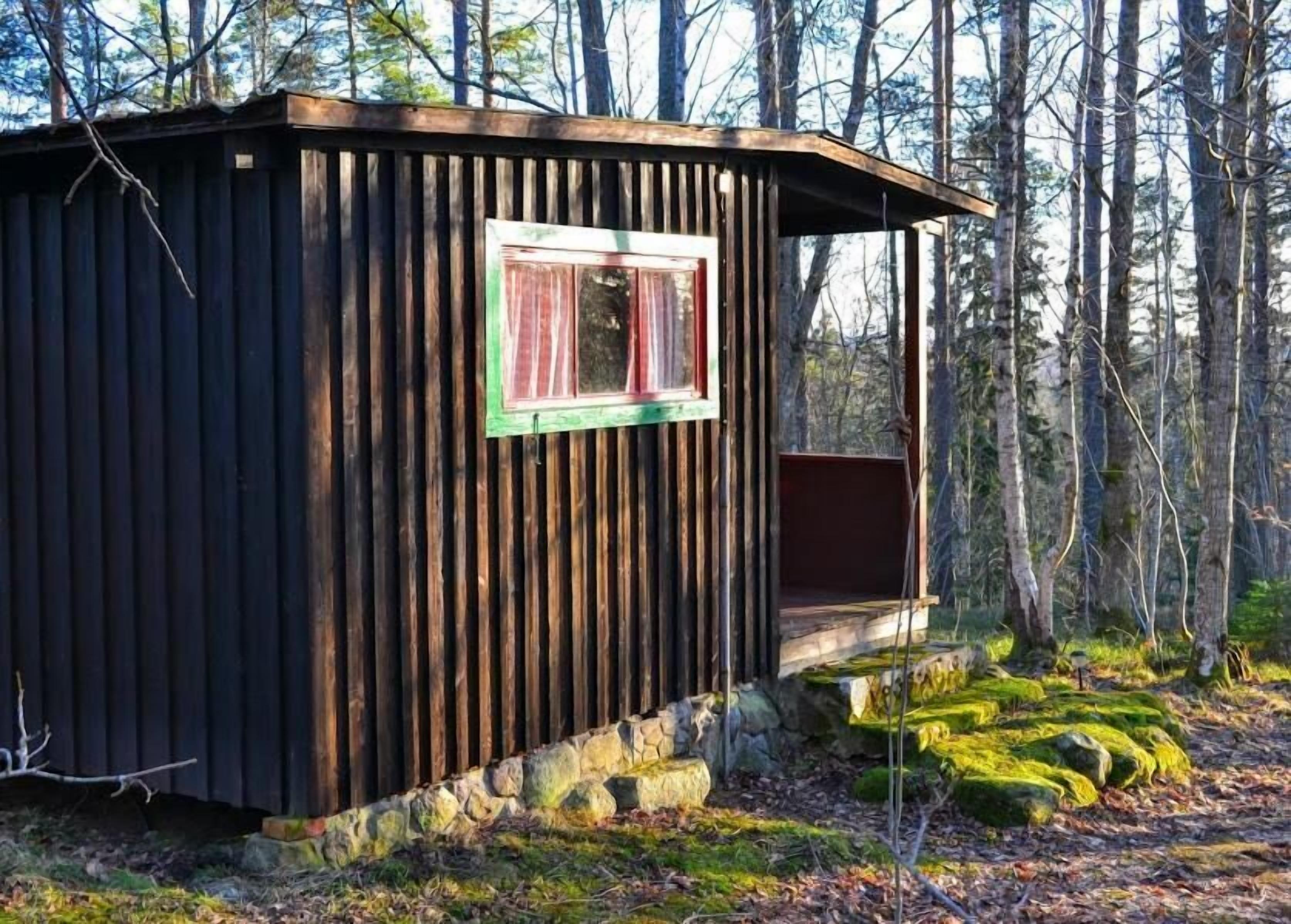 Una cabaña rústica con un único ventanal, rodeada de un bosque.