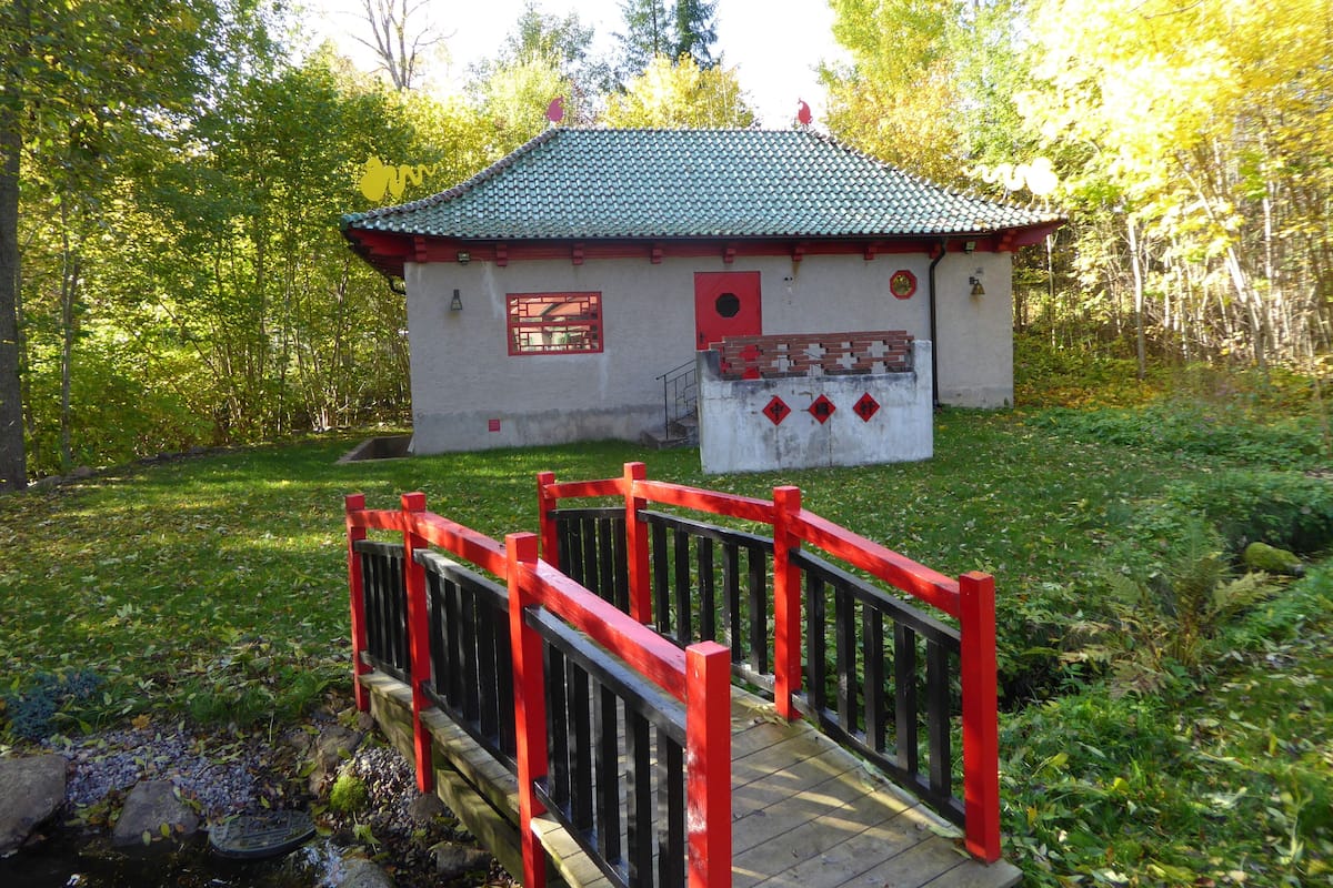 A small traditional building with a red roof and a wooden bridge leading to it.