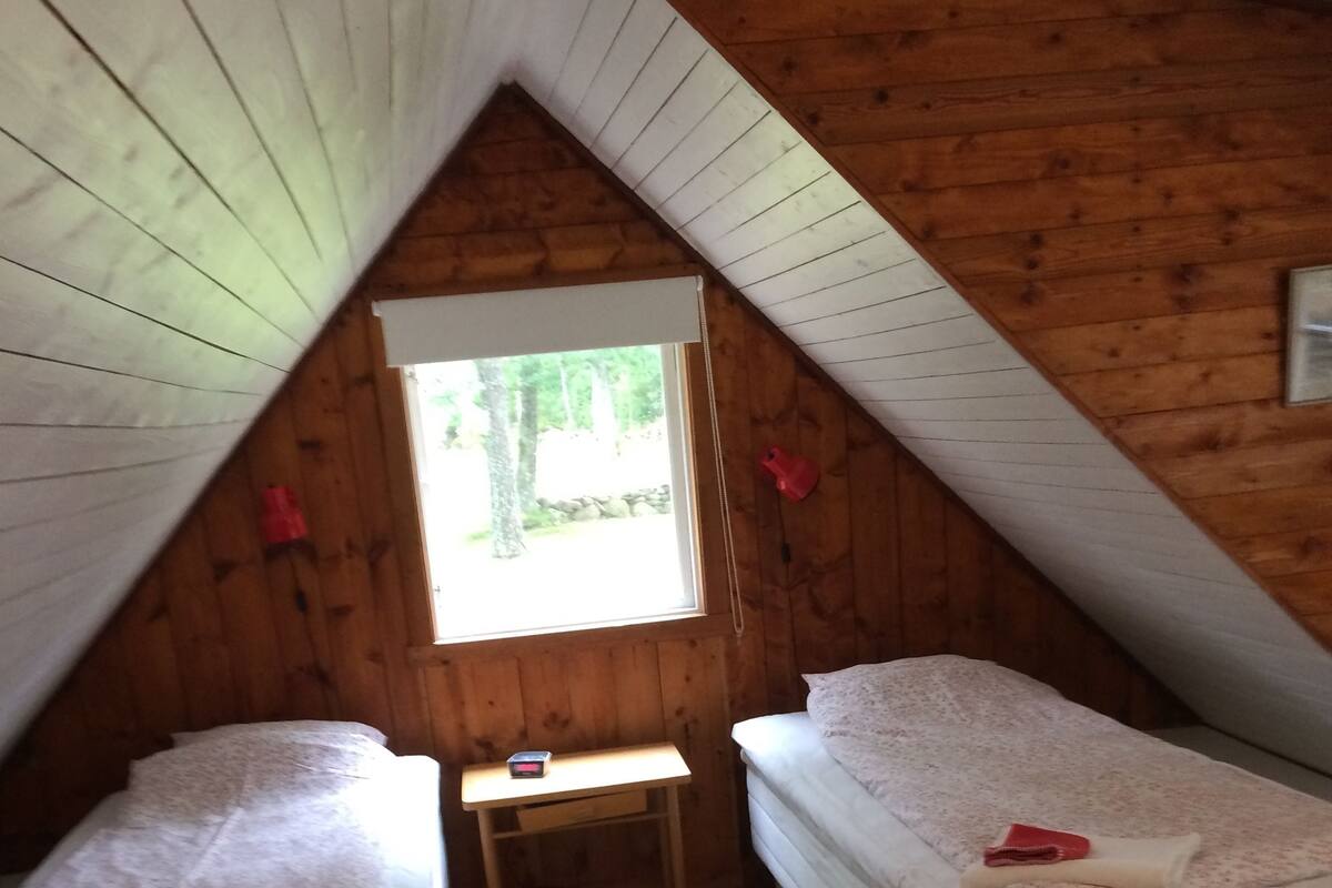A small, cozy attic bedroom with two single beds, a small desk, and a window providing natural light.