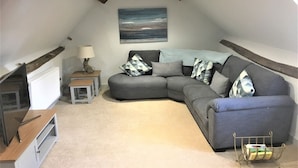 A cozy loft bedroom with a curved gray sofa, a small wooden side table, a lamp, and a painting on the wall. - Charming New Forest Escape Near Forest Walks & Coast (Fordingbridge)
