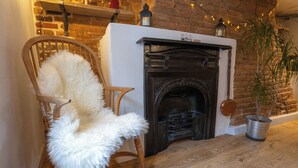 A cozy room with a wooden chair, a white fur chair, a fireplace, and a potted plant. - Charming New Forest Escape Near Forest Walks & Coast (Fordingbridge)