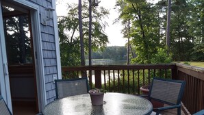 A round glass table with four chairs on a wooden deck, overlooking a lake and surrounded by trees. - Large, safe, WATERFRONT home in Idyllic setting with kayaks, bikes, &GARAGE use. (Reedville)