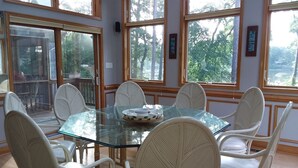 A dining area with a glass table surrounded by wicker chairs, large windows with views of trees, and a wooden deck outside. - Large, safe, WATERFRONT home in Idyllic setting with kayaks, bikes, &GARAGE use. (Reedville)
