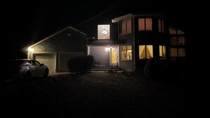 A two-story house with a garage, a driveway, and a lit front porch. - Large, safe, WATERFRONT home in Idyllic setting with kayaks, bikes, &GARAGE use. (Reedville)