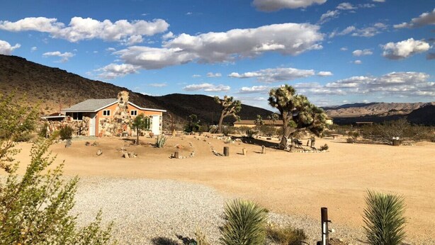 Paisaje desértico con un edificio de piedra, vegetación escasa y cielo despejado.