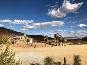 A desert landscape with a stone building, sparse vegetation, and a clear sky.