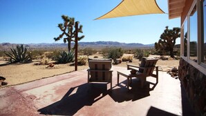 Un patio con mobiliario exterior, una vela de sombra grande y vistas a la vegetación desértica y montañas.