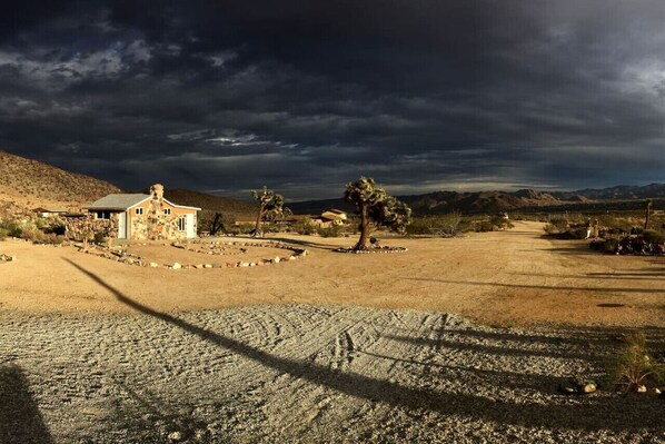 A desert landscape with a stone building, a tree, and a clear sky.