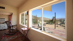 Una habitación con un amplio ventanal que da a un paisaje desértico, una mecedora y una pequeña mesa.