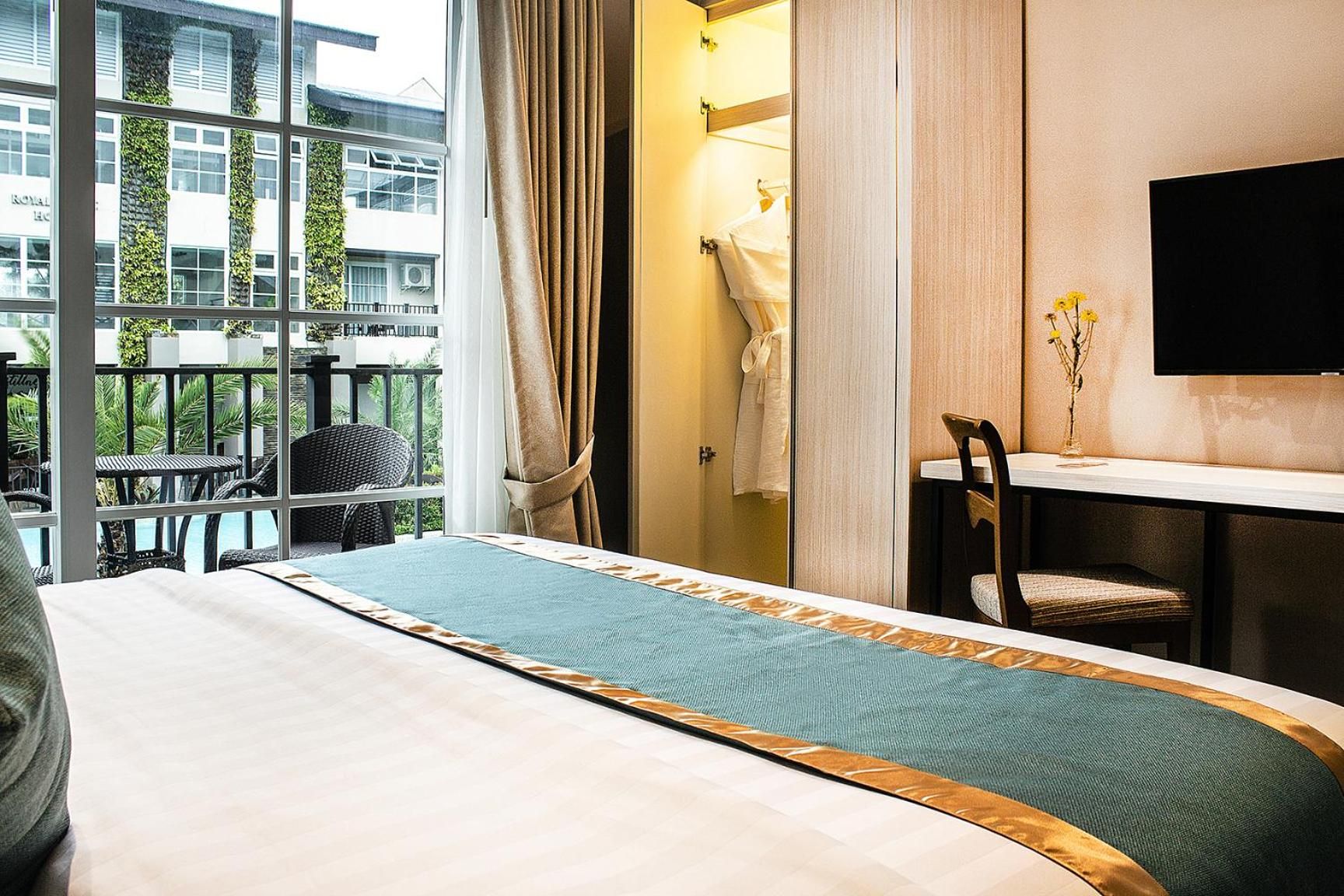 A hotel room with a bed, a desk, a chair, a TV, and a view of the outside.