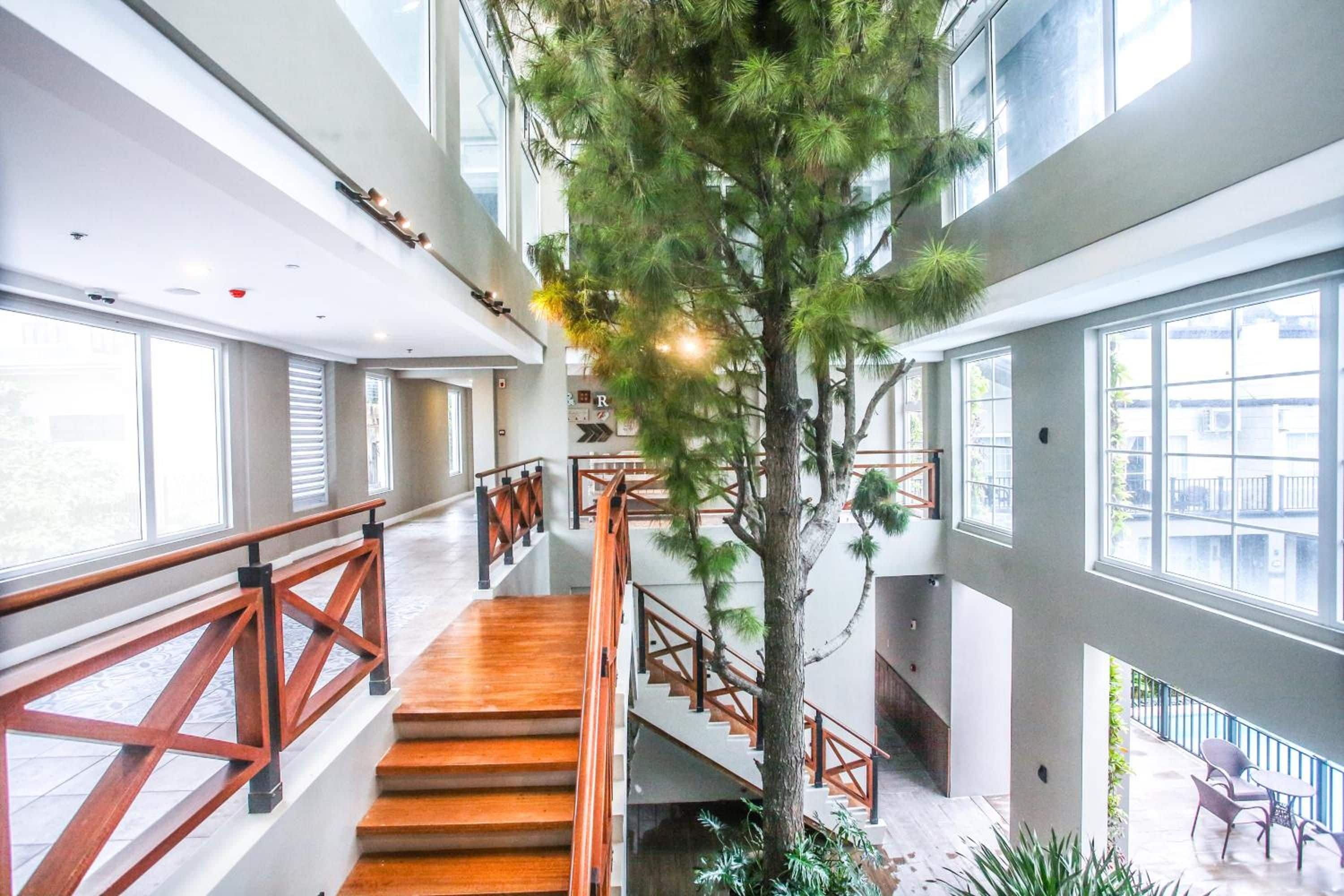 Un interior de varios niveles con escaleras de madera, barandillas de cristal y plantas de interior.