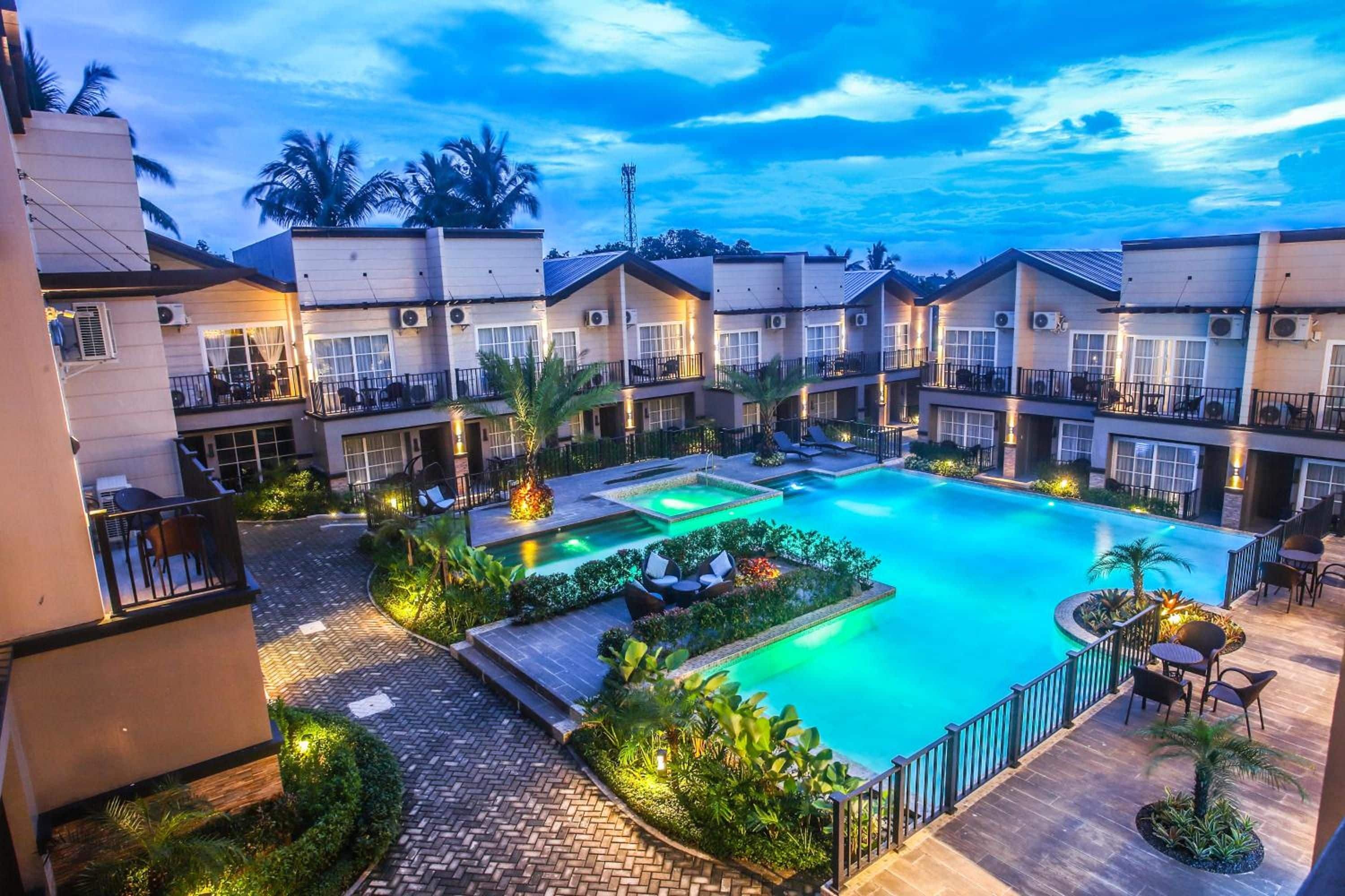 A hotel with multiple-story buildings, a central swimming pool, and outdoor seating areas.