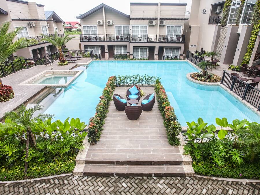 Un hotel con piscina, mobiliario exterior y abundante vegetación.