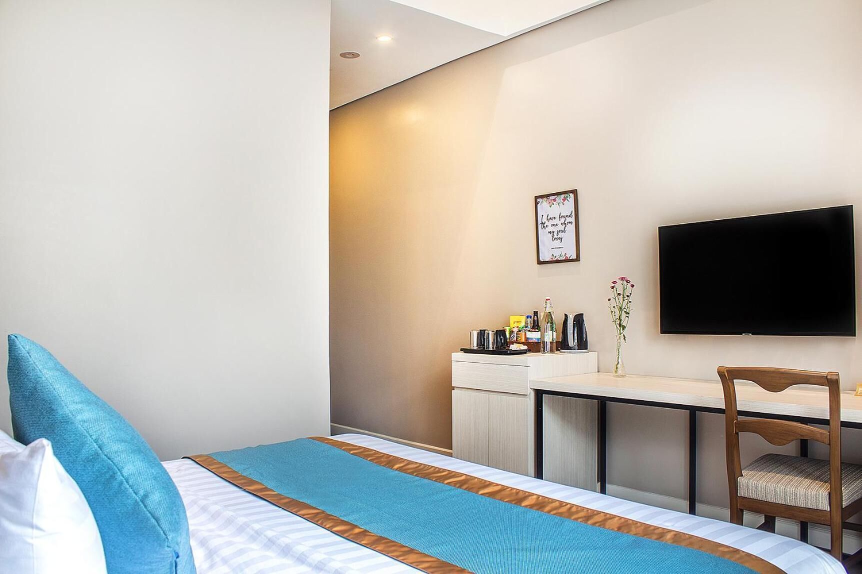 Habitación de hotel con cama, escritorio, silla, televisor de pantalla plana y una pequeña mesa con un jarrón de flores.