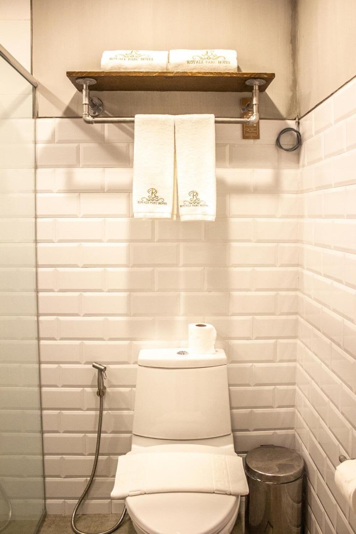 Une salle de bain avec des toilettes blanches, une douche et une étagère sur laquelle reposent deux serviettes portant l’inscription « ROYAL PARC HOTEL ».