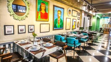 A restaurant with checkered flooring, teal and brown chairs, and framed artwork on the walls.