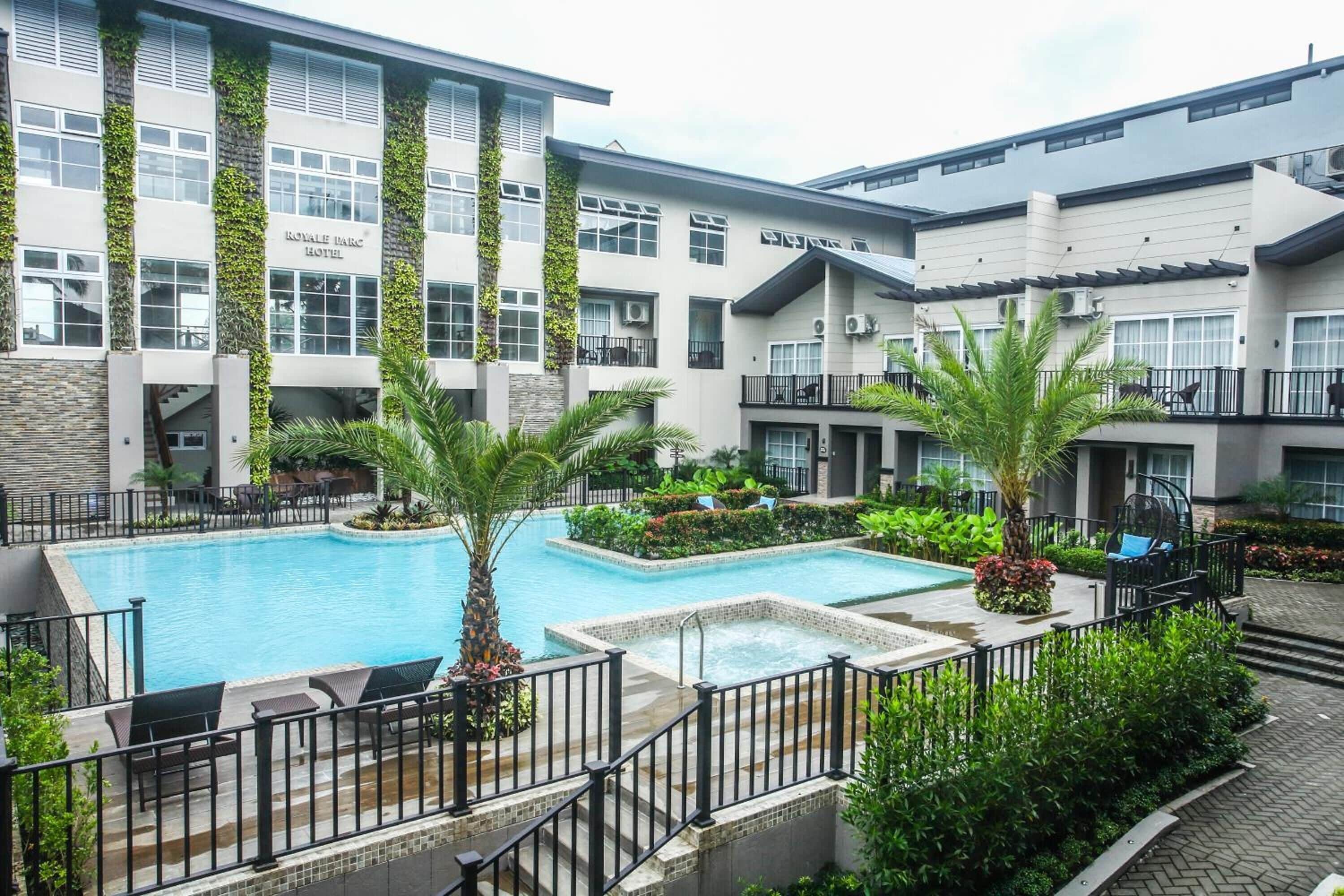 A hotel with a swimming pool, surrounded by greenery and a modern building facade.