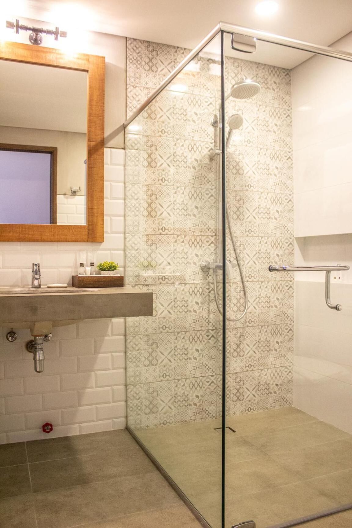 Un bany amb dutxa envidriada, un lavabo amb mirall i rajoles amb disseny.