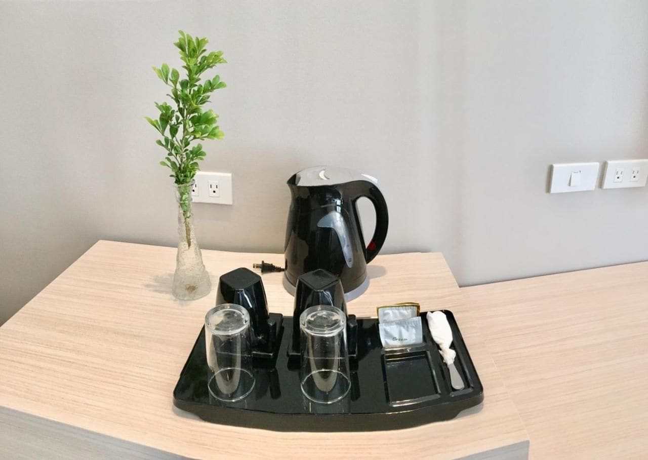 A coffee maker, a glass carafe, and a tray with cups and a spoon on a wooden table.